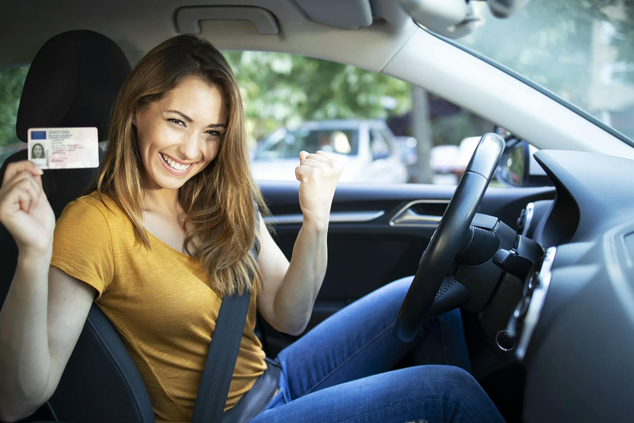 Mujer con una camiseta amarilla mostrando el carnet de conducir desde el asiento del conductor con una gran sonrisa